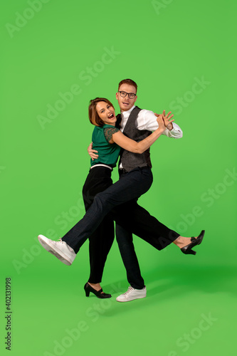 Fun. Old-school fashioned young woman dancing isolated on green studio background. Artist fashion, motion and action concept, youth culture, fashion returning. Young stylish man and woman.