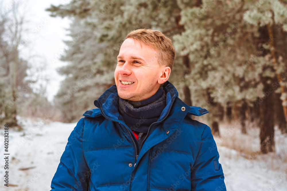Smiling happy young man in winter jacket in snowy winter forest, Christmas vacation Smiling happy young man in winter jacket in snowy winter forest, Christmas vacation