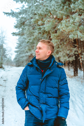 Smiling happy young man in winter jacket in snowy winter forest, Christmas vacation