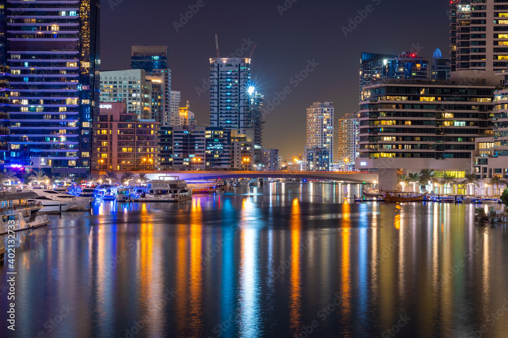 Night view to Dubai Marina panorama, reveals skyscrapers and beautiful bridge. Amazing colors reflect on the water. Luxury destination for tourists and residents. 