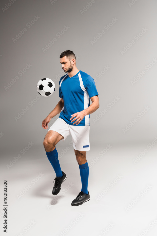 Bearded sportsman playing soccer on grey background