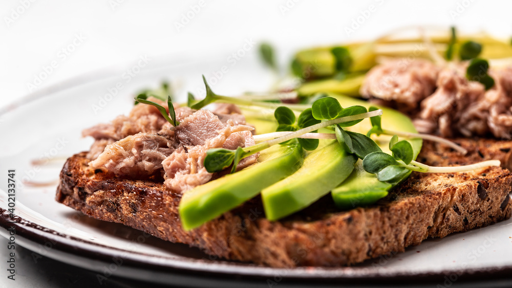 Tuna sandwiches with avocado and microgreen on wholemeal bread, wooden background. Tasty tuna sandwiches for breakfast or snack. Top view, flat lay, copy space