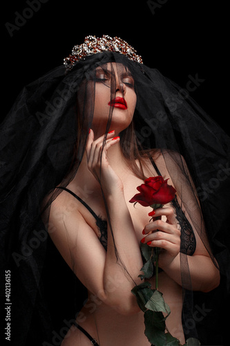 young beautiful girl in black headband and black veil in beautiful underwear with a scarlet rose in her hands on a black isolated background