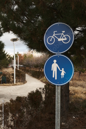 Compulsory footpath and compulsory bicycle path traffic signs together in the beginning of a pathway in a neighborhood with trees and bushes. 