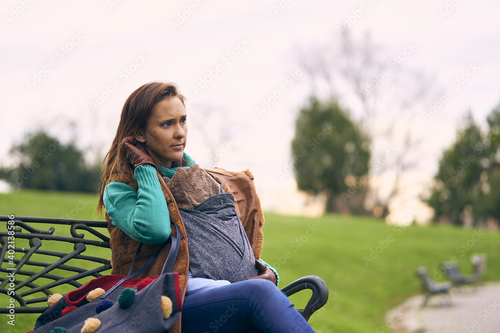 beautiful woman in sweater coat sitting on a bench in winter carrying her son on a cloudy day. maternity lifestyle concept beautiful woman in sweater coat sitting on a bench in winter carrying her son on a cloudy day. maternity lifestyle concept