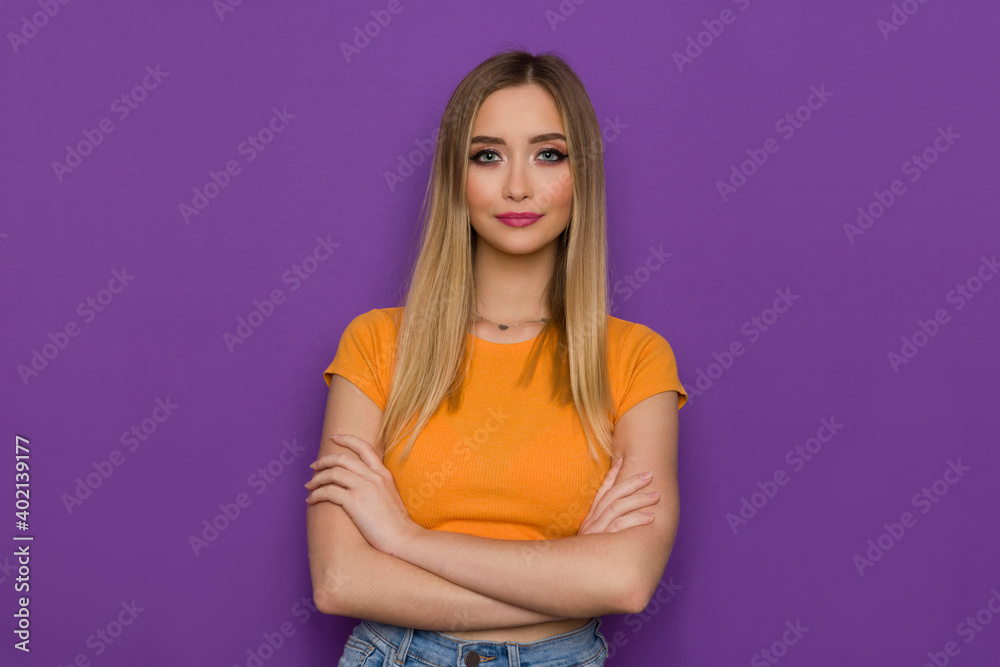 Young Blond Woman In Orange Top Is Posing With Arms Crossed Young Blond Woman In Orange Top Is Posing With Arms Crossed