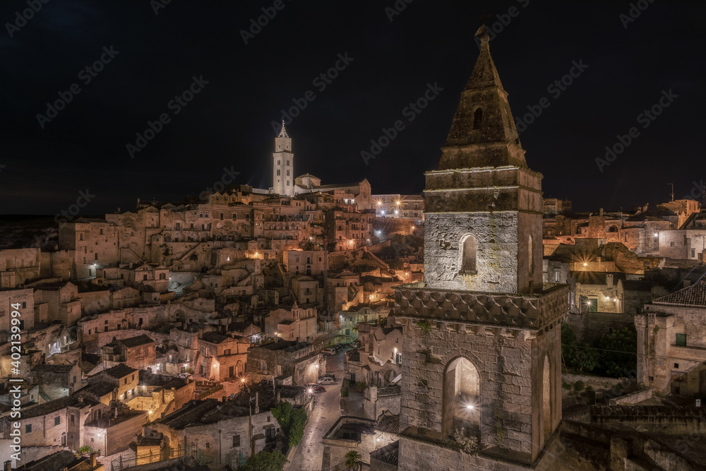View of the Sassi of Matera at night. The tower in the foreground is the bell tower of the Church of San Pietro Barisano, the tower on the second floor is the bell tower of the Pontifical Basilica