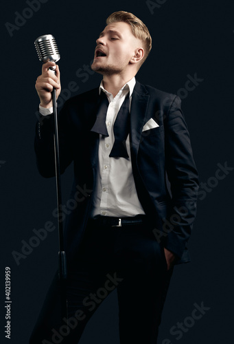 Handsome singer in elegant tuxedo and bow tie with vintage microphone