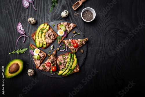 Open avocado sandwiches with tuna on whole grain bread on dark background. banner, catering menu recipe place for text, top view