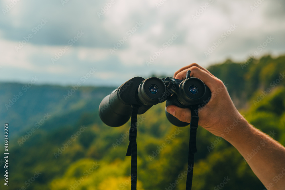 Hands holding binoculars on mountains forest nature background, looking through binoculars, travel, search and search concept. Hands holding binoculars on mountains forest nature background, looking through binoculars, travel, search and search concept.