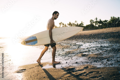 Fit young guy with surfboard walking on sandy beach