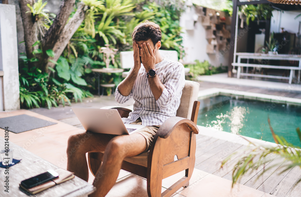 Young man covering face with hand while working