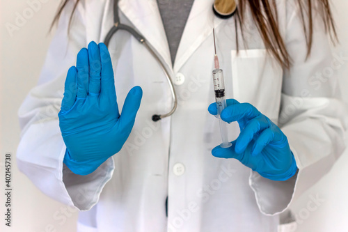 Young female doctor in blue gloves and a respirator mask for protection holds a vaccine for injection and gesture STOP sign. Stop virus. Syringe in doctor hand and sign stop. Health and people concept