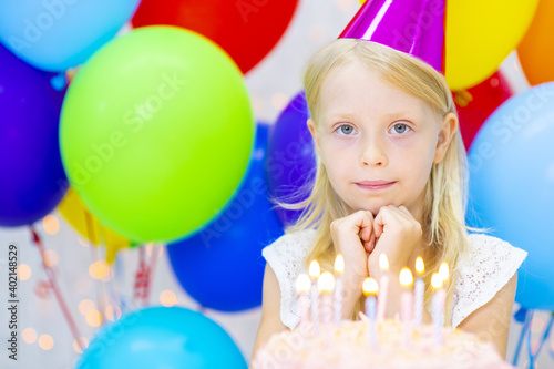 Little girl in a party cap with cake in honor of her birthday