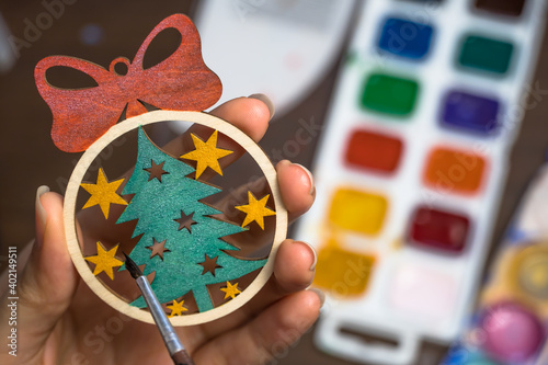 Paint the Christmas tree toy with colors. Create a decoration for the new year at home. Hobbies and creativity, handmade. The artist draws on a wooden toy. Art, creation. Decorate the Christmas ball