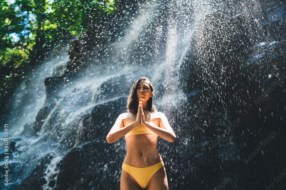 Thoughtful slim woman praying near waterfall