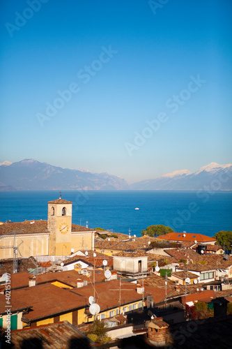 Aerial view of the snow-capped Italian alps, Garda lake and small european buildings with orange tiled roofs, towers and chimneys. Panorama of Desenzano del Garda, Lombardy, Italy.