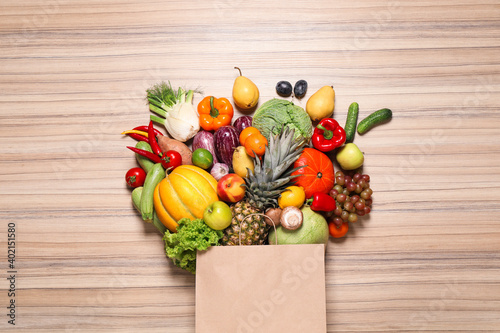 Paper bag with assortment of fresh organic fruits and vegetables on wooden table, flat lay