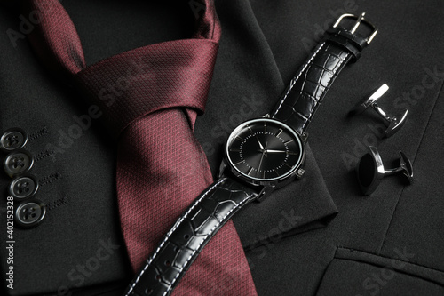 Luxury wrist watch, tie and cufflinks on black jacket, closeup photo