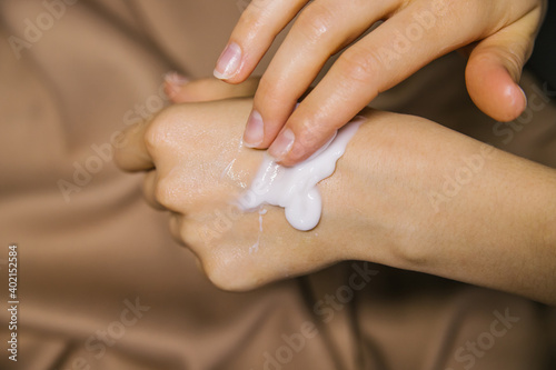Women s hands on a beige fabric background.A woman smears cream on her hands. Care and care of the skin.