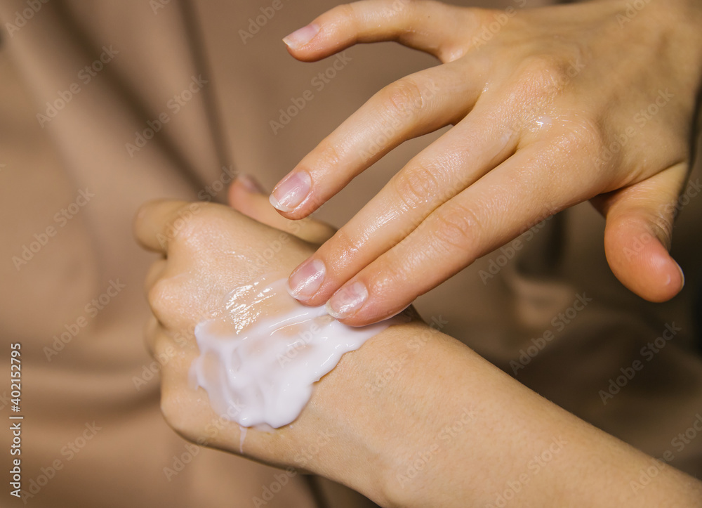 Women's hands on a beige fabric background.A woman smears cream on her hands. Care and care of the skin. Women's hands on a beige fabric background.A woman smears cream on her hands. Care and care of the skin.