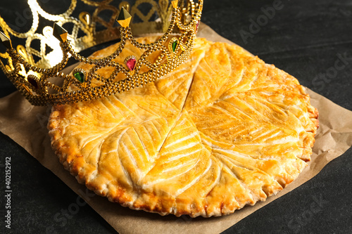 Traditional galette des Rois with decorative crown on black table, closeup
