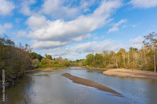 A small beach for fishing and relaxing on the banks of the Neuse River in Raleigh, North Carolina in autumn surrounded by trees near the Milburnie Dam bridge