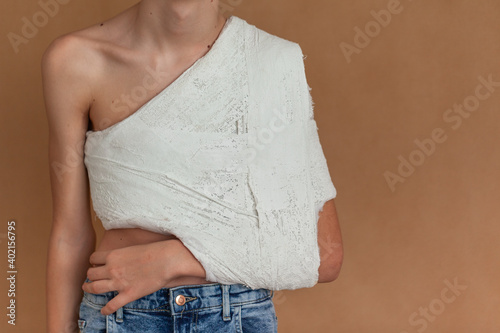 Yuong boy on a beige isolated background with a back, collarbone or shoulder injury. Medical care for fracture of the clavicle. photo