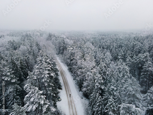 Aerial view of road and man in winter night forest. Forest work Establishing shots in the winter landscape. Icy road. Snow covered nature. Spruce forest Latvia Winter background from above. © Girts