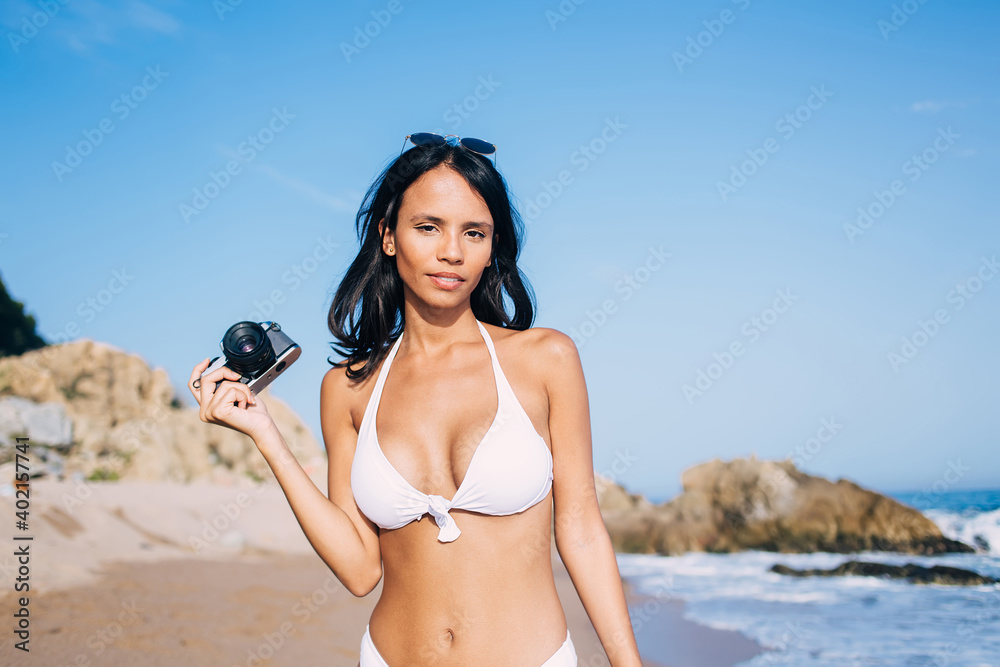 Half length of young woman with vintage camera in hand posing during  tanning leisure at seashore coastline, charming female amateur using retro  technology during summer vacations at Bahamas foto de Stock