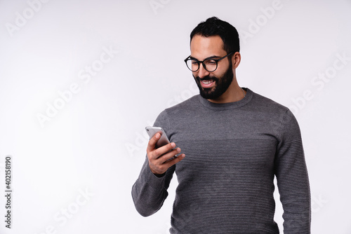 Nice-looking young Arabian man in casual clothes using mobile phone isolated over white background © InsideCreativeHouse