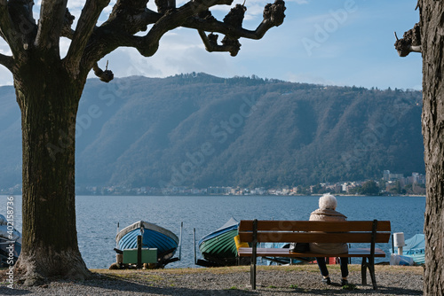 Elderly woman sits on the Bissone promenade on a warm winter day and enjoys the lake Ceresio view. Canton Ticino. Switzerland photo