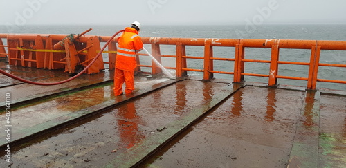 a sailor washes the deck of a ship with the pressure of sea water from a fire hose photo