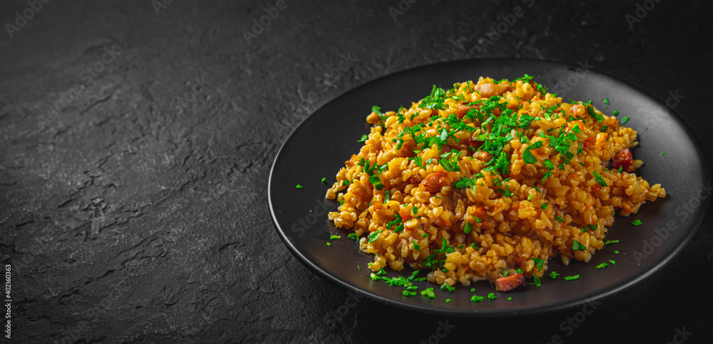 Bulgur with vegetables and meat on black plate on Dark grey black slate background Bulgur with vegetables and meat on black plate on Dark grey black slate background