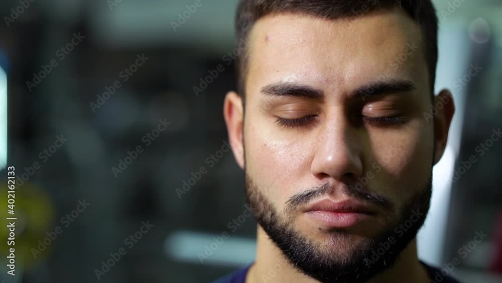 Handsome man with beard opening eyes and looking at camera, sports equipment on blurred background. Closeup of athlete relaxing after training. Concept of sport Handsome man with beard opening eyes and looking at camera, sports equipment on blurred background. Closeup of athlete relaxing after training. Concept of sport