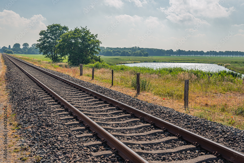 Rusty railway tracks diagonally in the picture. The rails are mounted on concrete sleepers. There are pebbles between the rails. The photo was taken in the Dutch spring season.