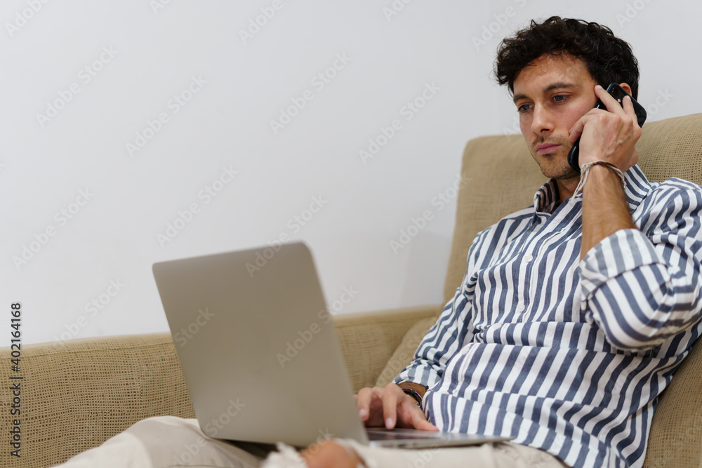 Portrait of a man working with a laptop while talking to the mobile on the couch Portrait of a man working with a laptop while talking to the mobile on the couch