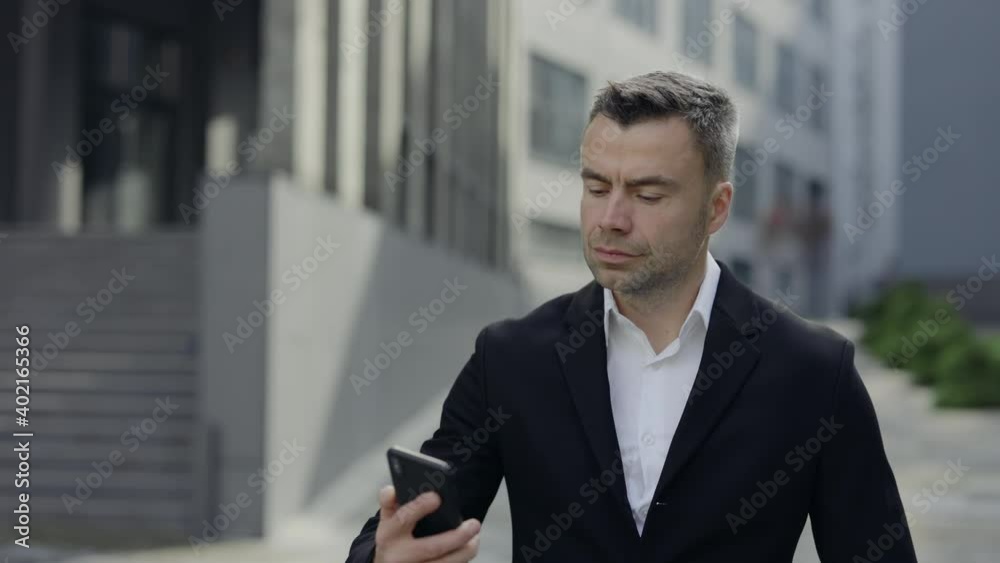 Crop view of successful mature man in classical suit and shirt talking and shaking head while answering call. Businessman in 40s having conversation on smartphone while walking at street. Crop view of successful mature man in classical suit and shirt talking and shaking head while answering call. Businessman in 40s having conversation on smartphone while walking at street.