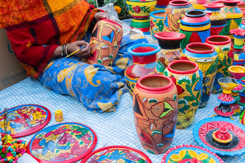 Female Indian artist painting colorful terracotta pots, works of handicraft, for sale during Handicraft Fair in Kolkata.