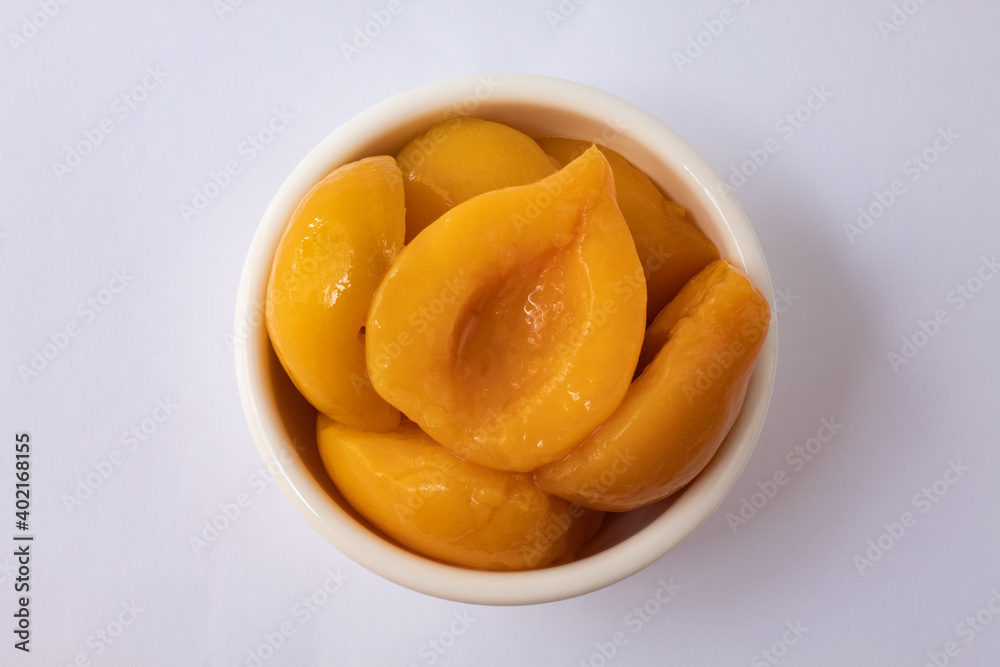 Top view of halved peaches in syrup in white bowl