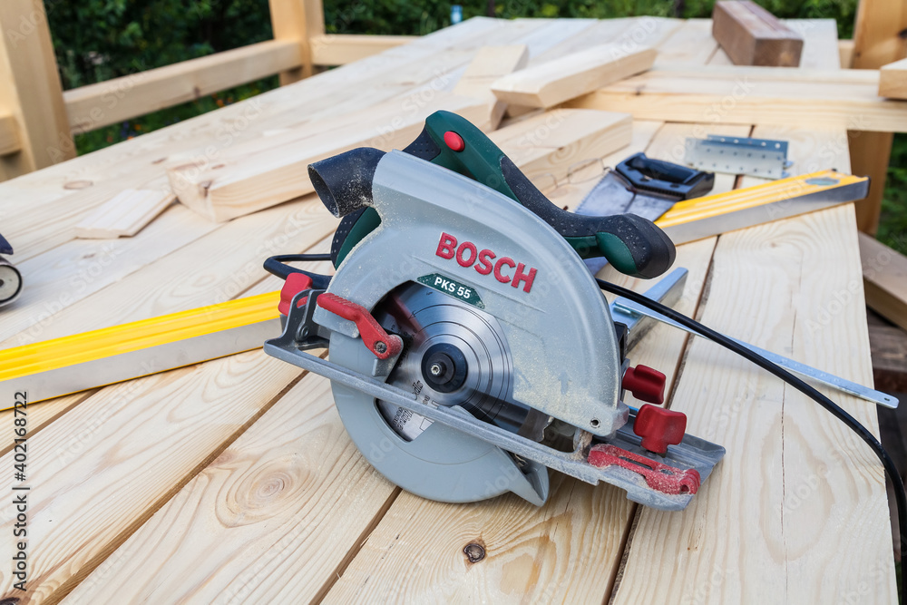 Close-up of a modern new electric hand saw Bosch PKS 55 with a green  plastic case and a metal blade on a wooden beam during the construction  work of a carpenter. Stock