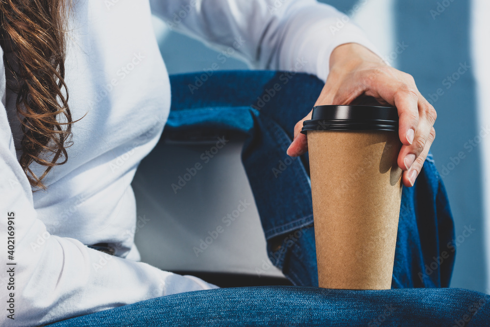 Naklejka premium Young woman in white t shirt and denim jeans holds disposable coffee cup. Youth, modern lifestyle. Coffee break, cosy relaxing moment. 