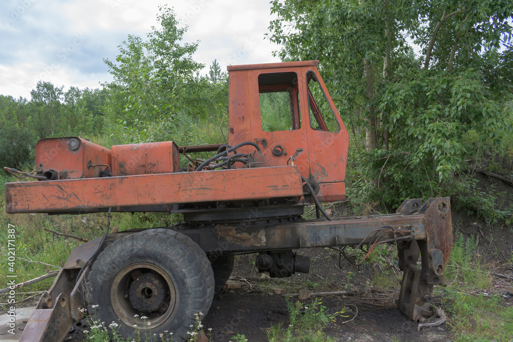 Old skeleton of a truck crane. Frame with wheels and cab. Profile view. Green Forest.