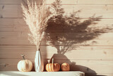 Pampas grass in white vase with pumpkins on wooden background with bright sunlight. minimalistic pampa concept.
