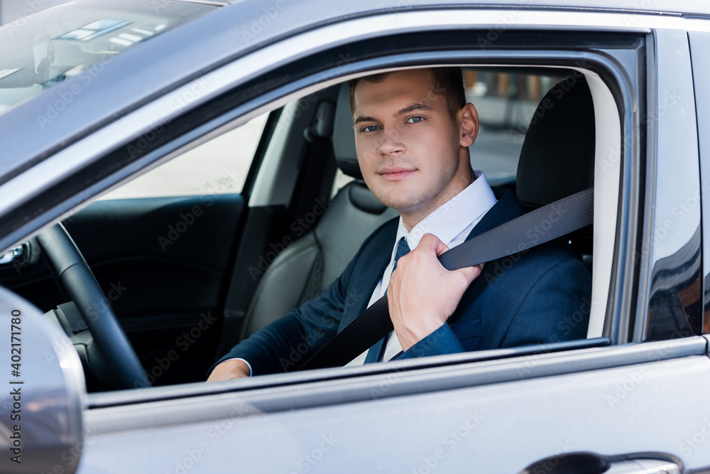 Businessman in formal wear holding safety belt in car and looking at camera. Businessman in formal wear holding safety belt in car and looking at camera.