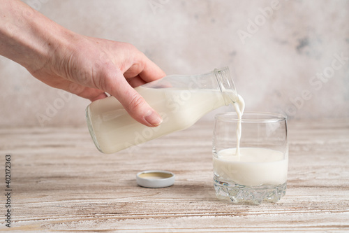 Pouring fresh milk from glass bottle to glass. Hand holding a bottle with milk on wooden table photo