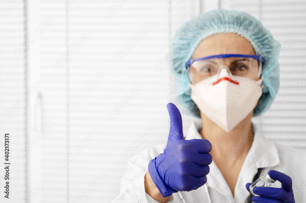 Portrait of happy smiling caucasian female doctor in mask glasses gloves and hat shows thumb up on white window background Portrait of happy smiling caucasian female doctor in mask glasses gloves and hat shows thumb up on white window background