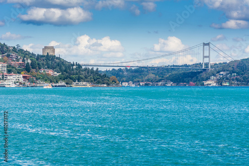 Modern builings and Rumelian Castle, and Fatih Sultan Mehmet Bridge across the Bosphorus strait in Istanbul Turkey from ferry on a sunny day with background cloudy sky © zz3701