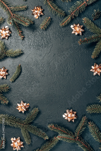 Creative frame made of Christmas fir branches, gold bow on a dark green background. Xmas and New Year theme. Flat lay, top view, copy space