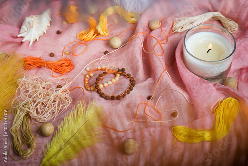 Two handmade shamballa bracelets made of rudraksha and amber beads on a pink tissue with scattered beads, threads, feathers and a candle photo